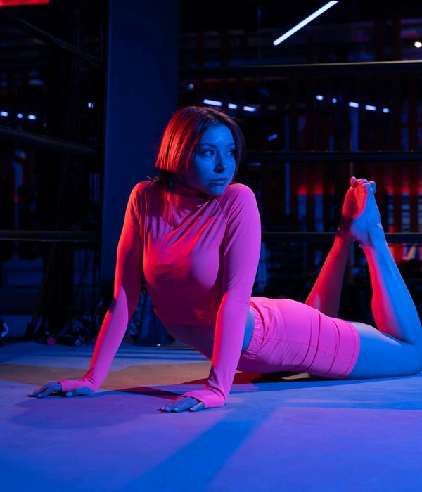 Woman in a calm yoga pose in a dark room with neon blue light.